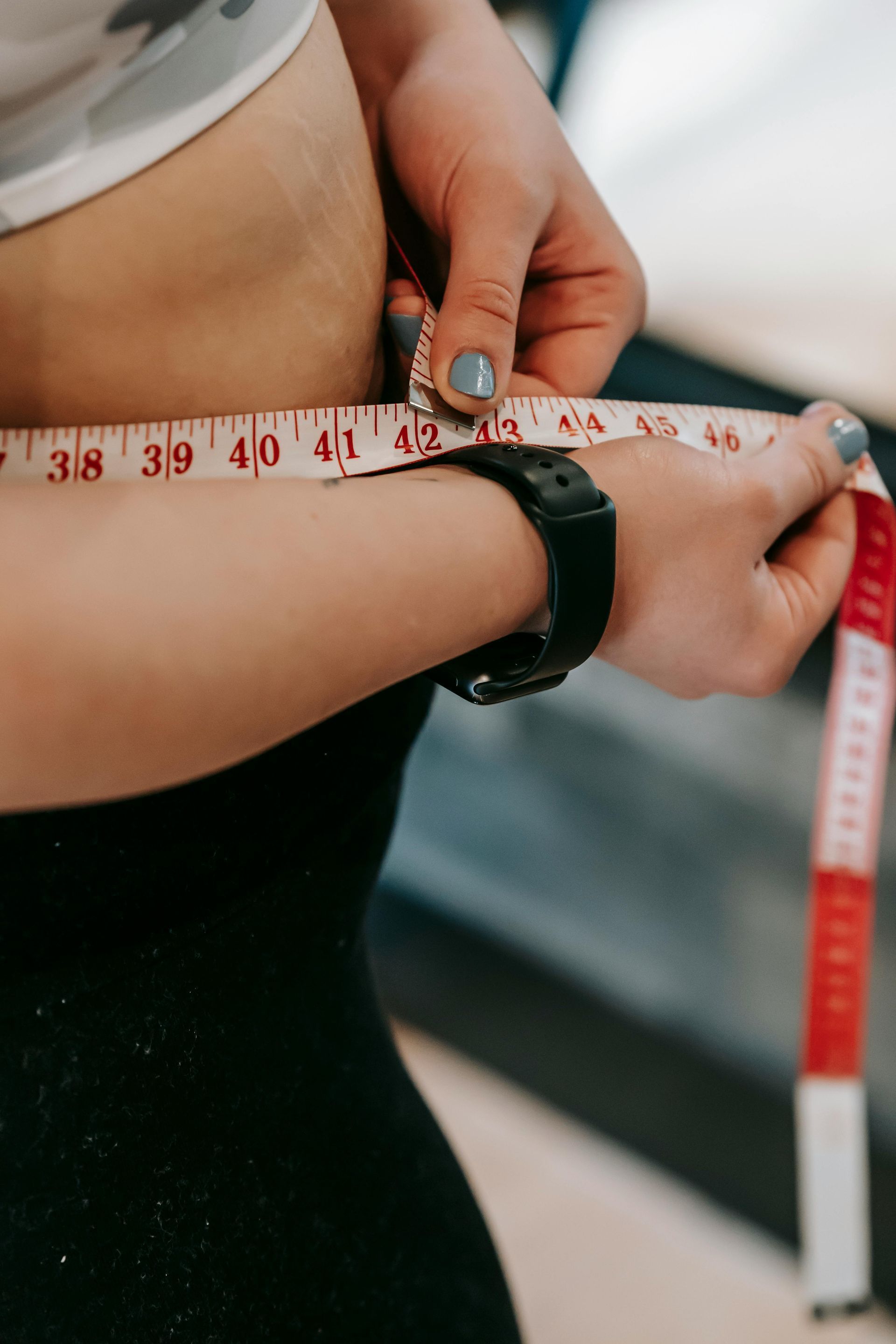 Person measuring waist with a tape measure, wearing black clothing.