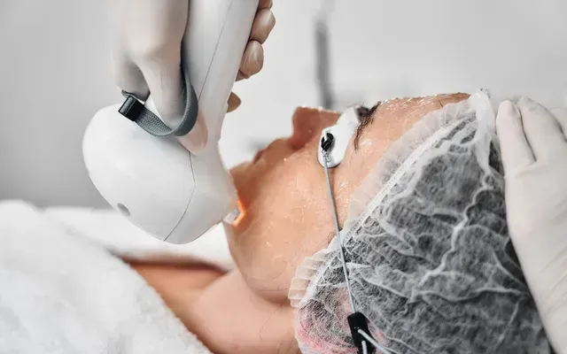 Cosmetic facial treatment with handheld device on a person covered in white protective cap and towel