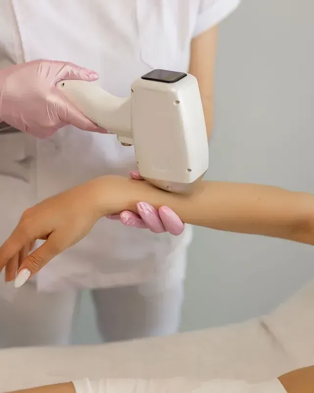 Gloved practitioner using a handheld device on a person’s forearm during a cosmetic skin treatment