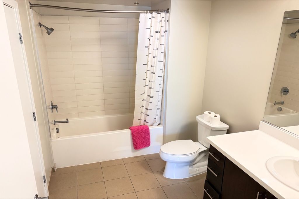 Bathroom with tub, shower curtain, toilet, sink, and white tile walls.