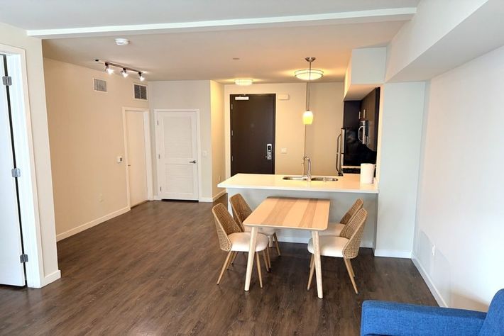 Open-plan living and dining room with hardwood floors, a white table, chairs, and a kitchen bar.