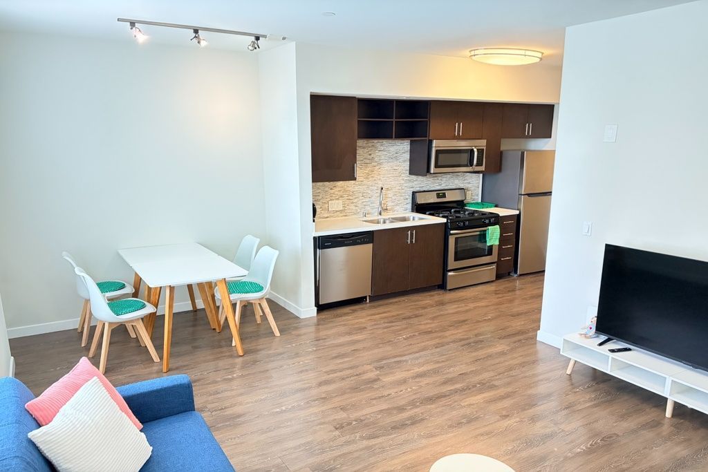 Open-plan living room and kitchen with white walls, wood floors, dining table, blue sofa, and black appliances.