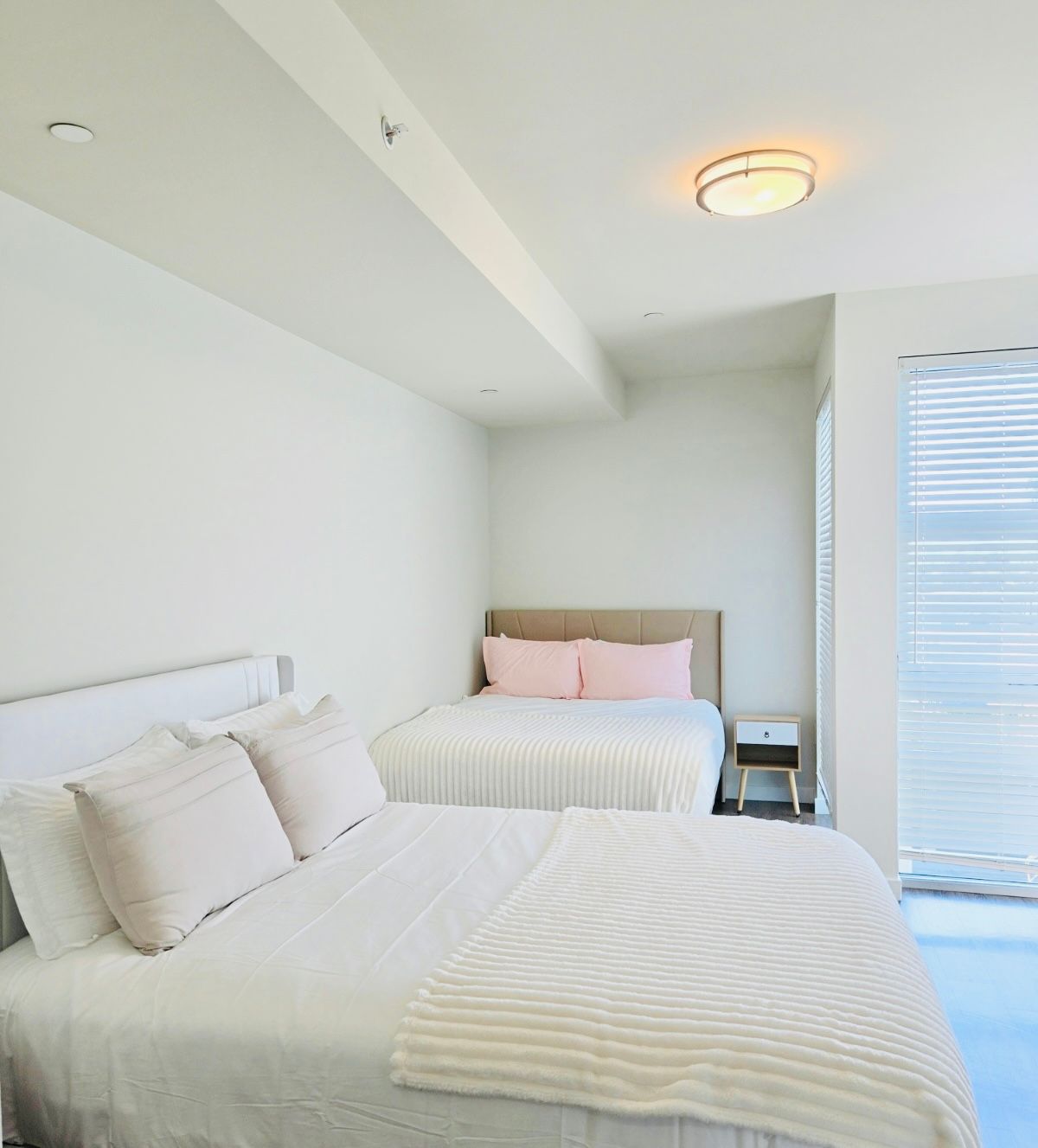 Bright white bedroom with two neatly made single beds and a window with blinds