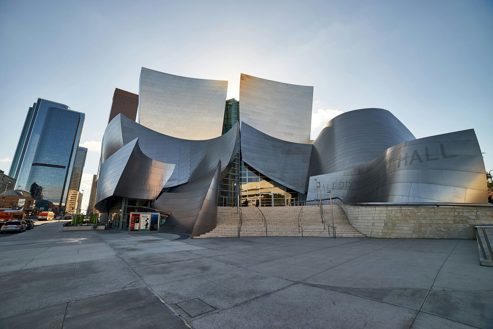 Modern metallic building with curved silver panels and glass entrance in a city plaza at sunset