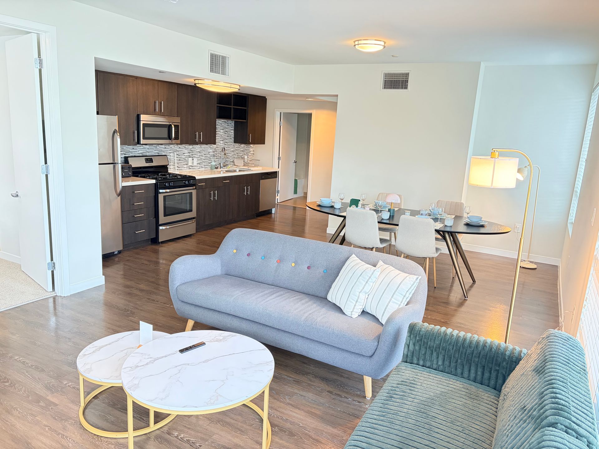 Open-plan apartment living room with sofa, coffee tables, dining area, and kitchen in the background