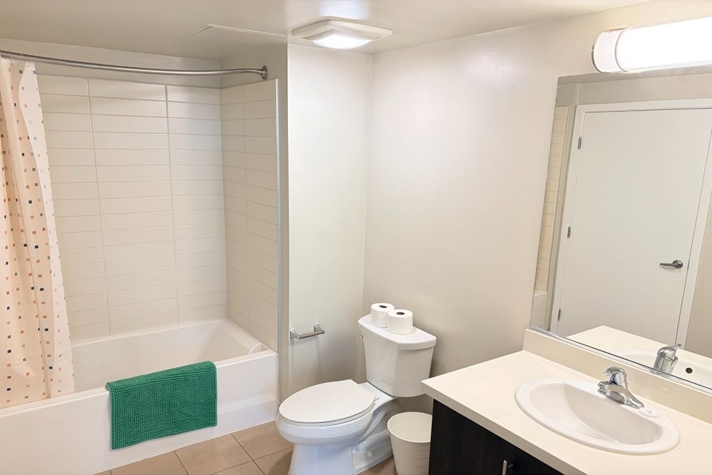 Bathroom with tub, toilet, and sink, white walls, and a green towel on the tub.