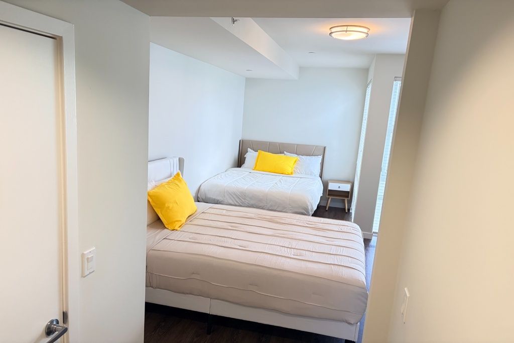 Small bedroom with two beds, yellow pillows, and white walls, viewed from the doorway