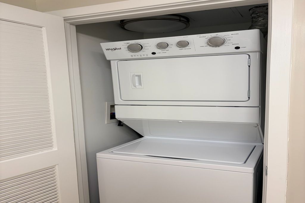 Stacked washer and dryer in a closet, with the dryer door open and a vent above.