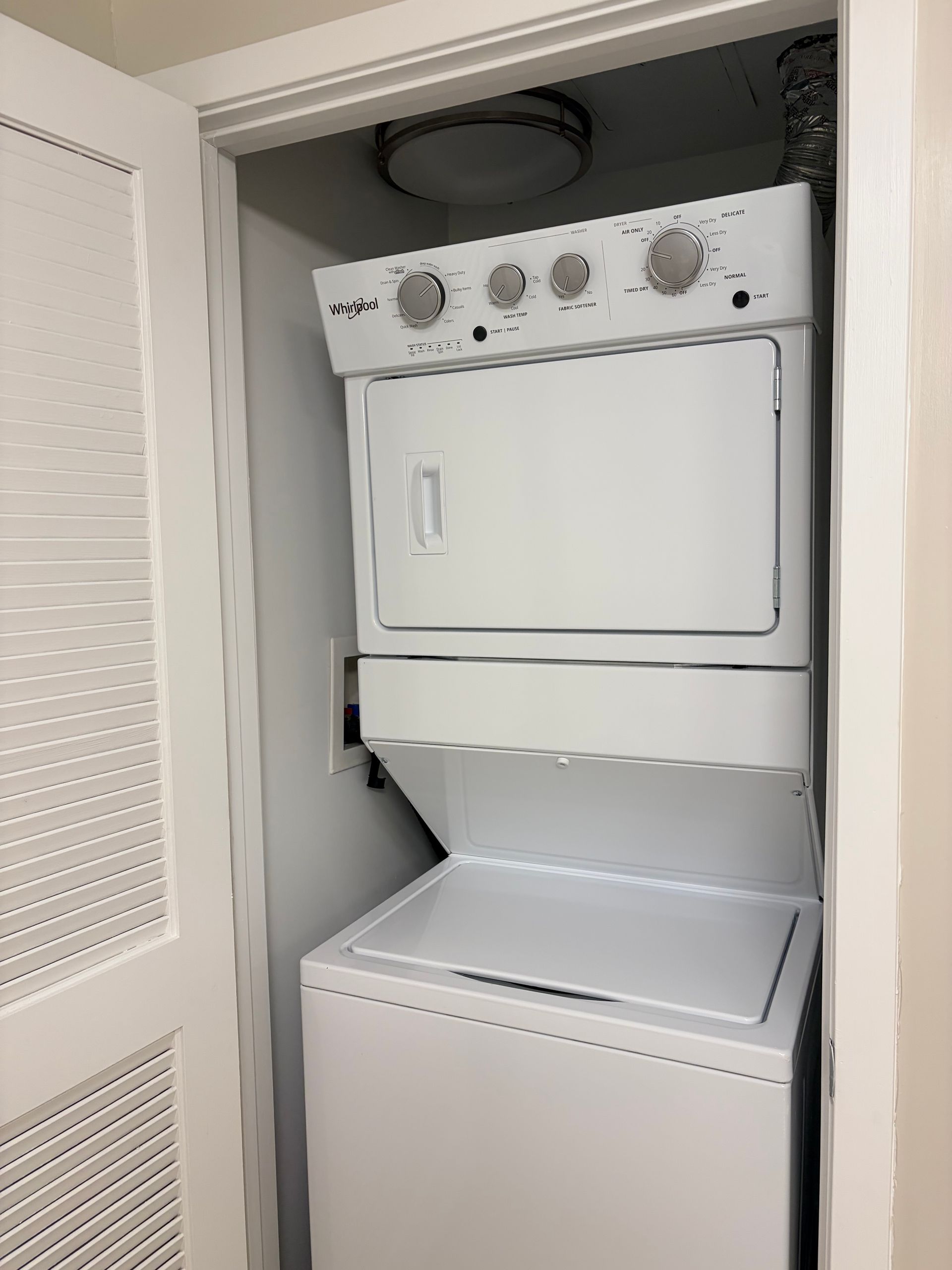 Stacked washer and dryer in a closet with white doors and shelves above and below