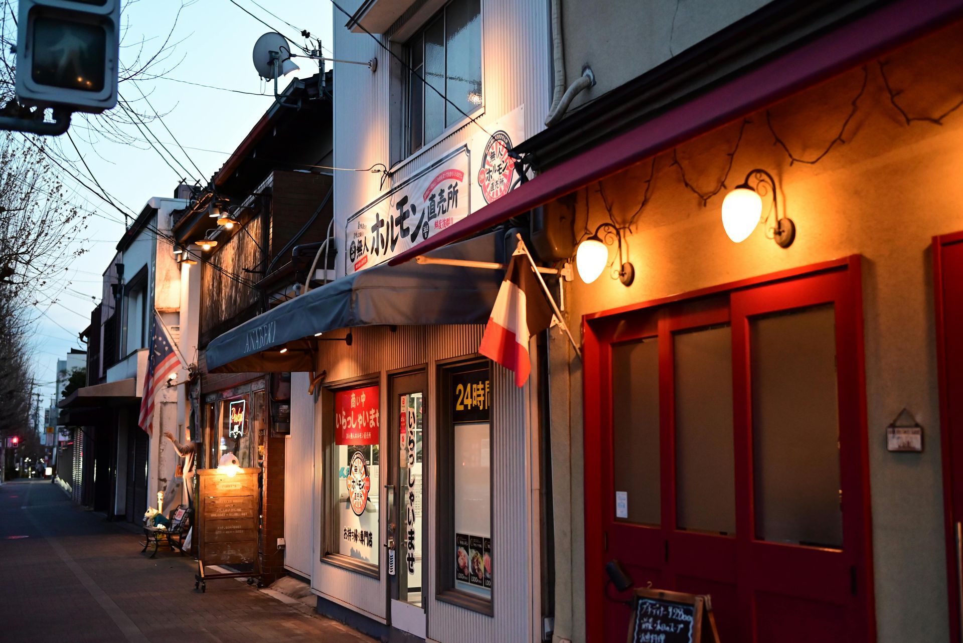Quiet street with warmly lit storefronts and red doors at dusk