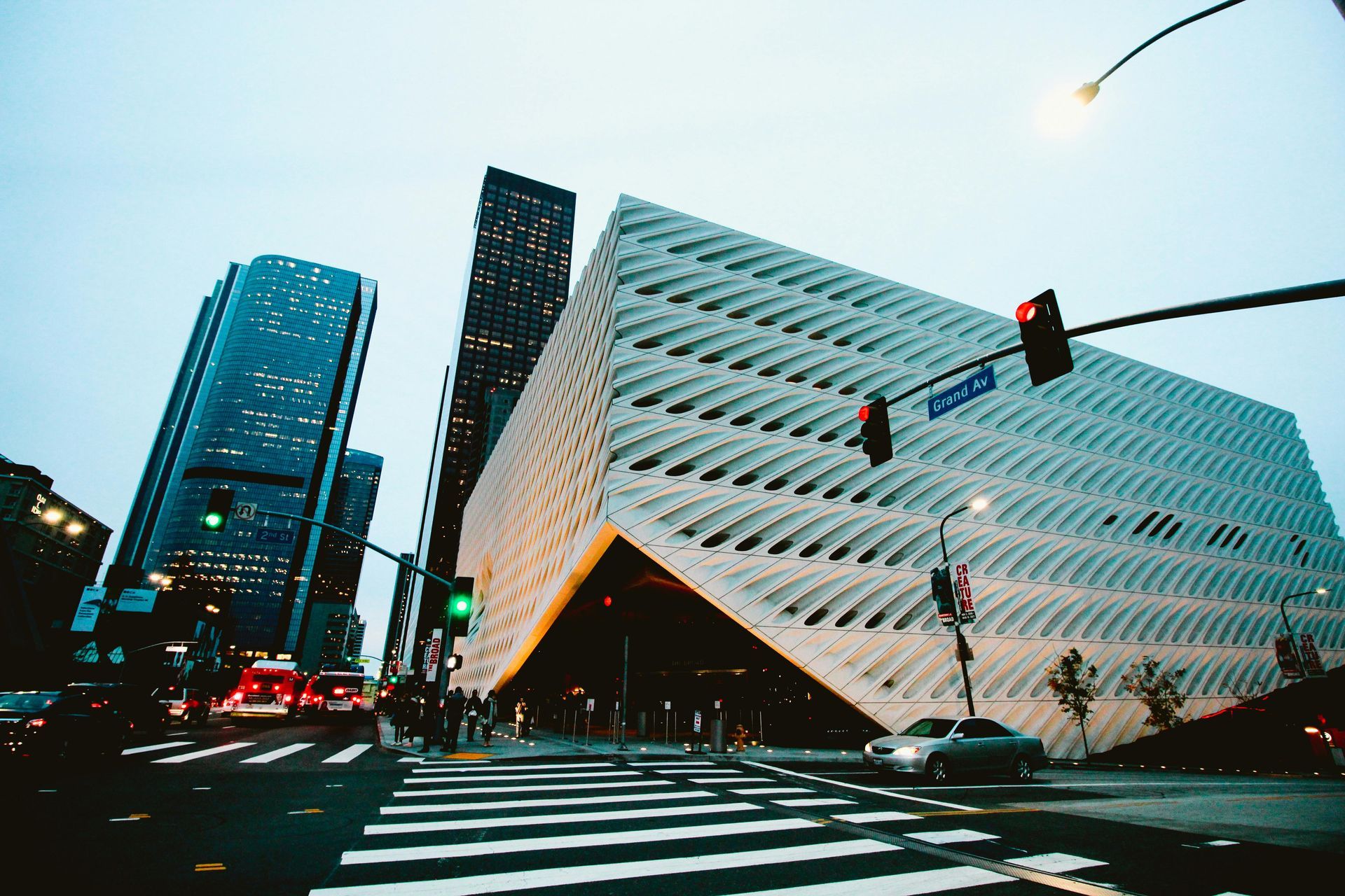 Modern angular office building at a city intersection with traffic lights and crosswalk at dusk