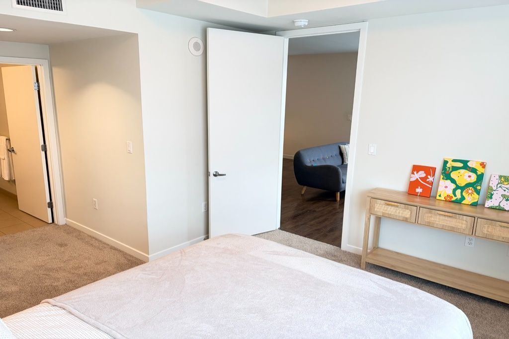Bright bedroom with open white door, beige carpet, and a wooden table with colorful items.