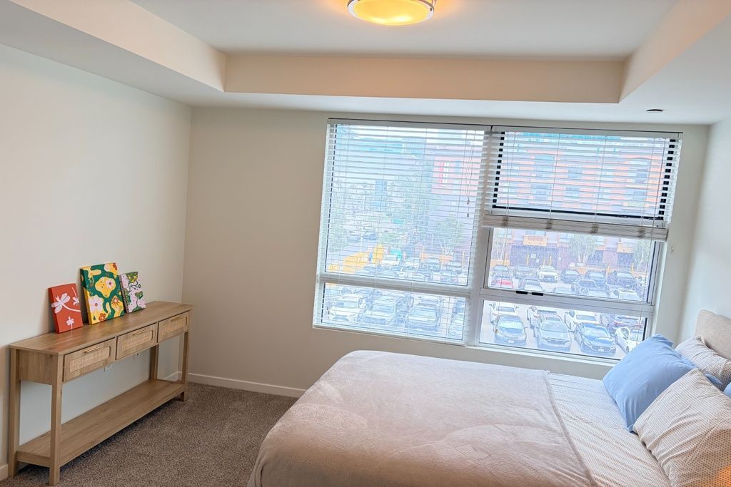 Bright bedroom with a bed, window light, and a small wooden table with books and decor.