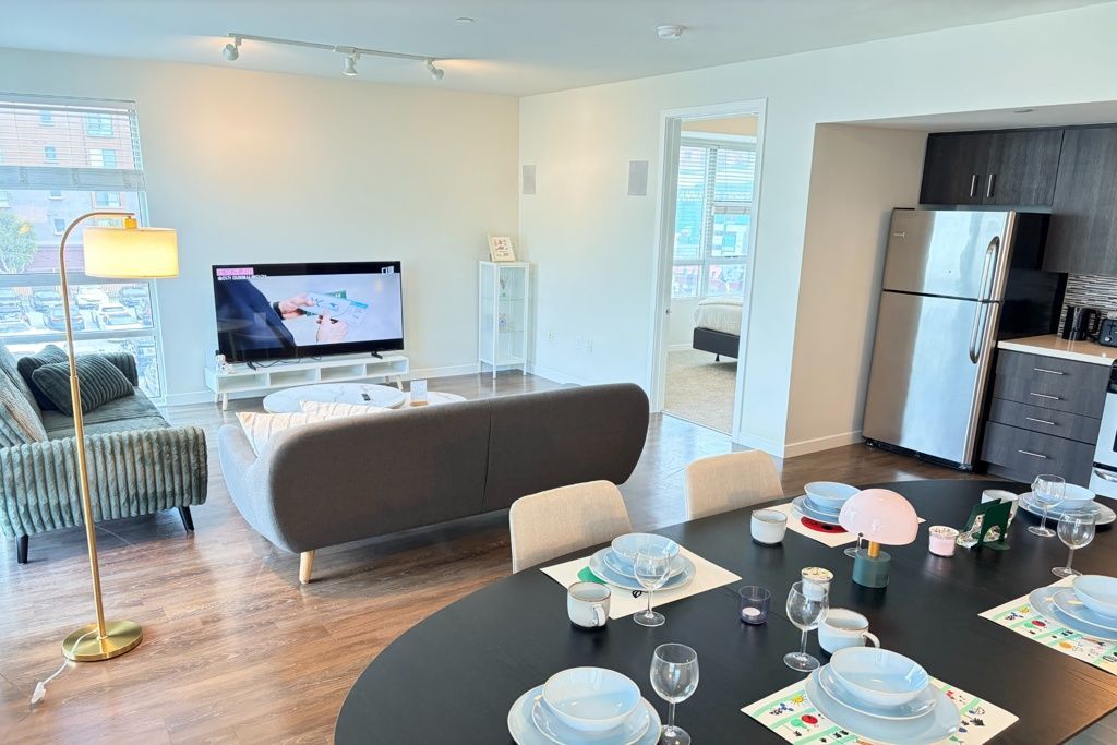 Modern open-concept living room and kitchen with dining table, sofa, TV, and stainless steel appliances