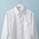 Camisa blanca de manga larga con botones, colgada en una percha sobre un fondo azul claro