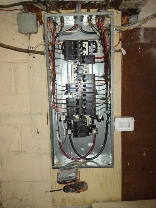 Open electrical breaker panel with exposed wiring in a basement wall