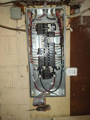 Open electrical breaker panel with exposed wiring in a basement wall