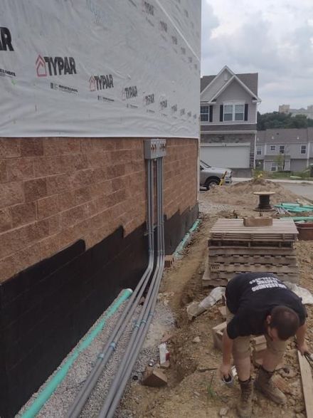 Construction worker installing siding and foundation wrap on a house exterior, with tools and materials beside him