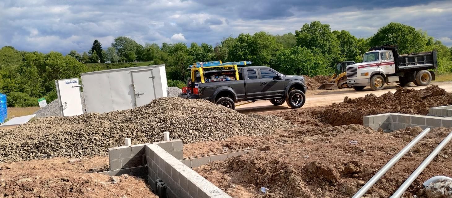 Construction site with black and white work trucks on a muddy lot near concrete foundations