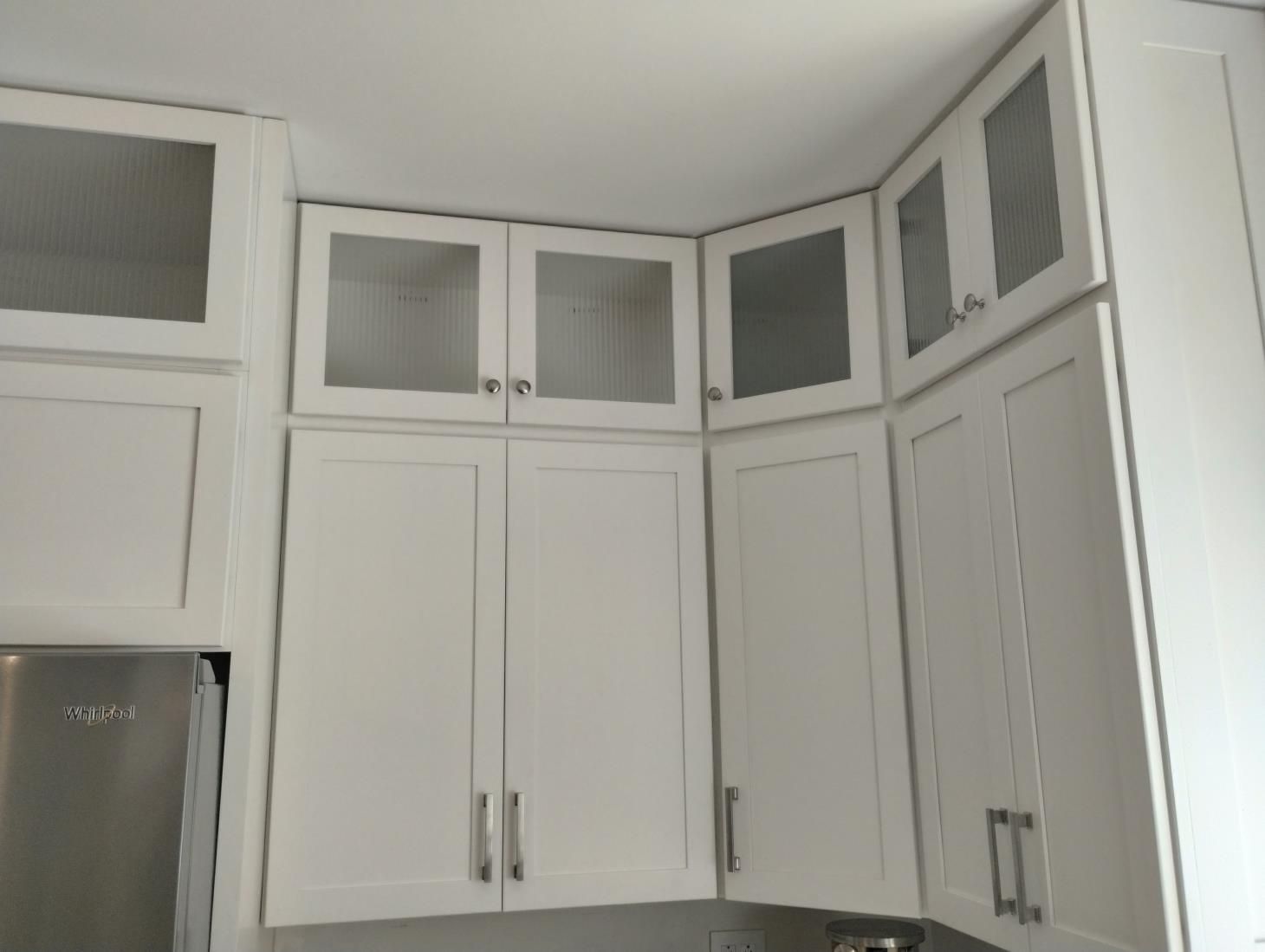 White kitchen cabinets with glass-front upper doors and stainless steel refrigerator.