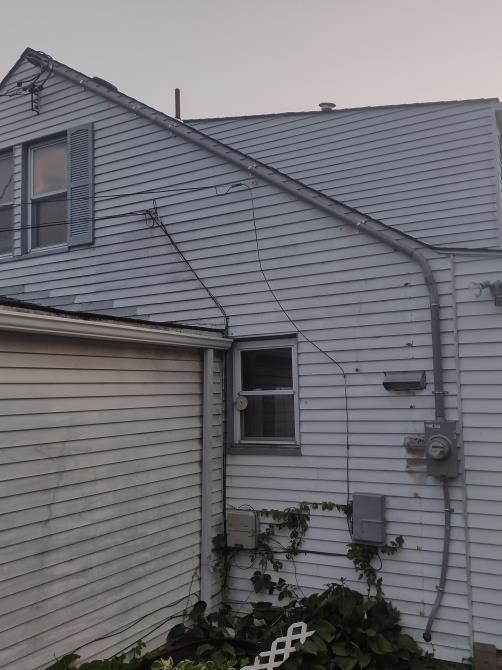 White house exterior with gray siding, sloped roof, small window, and vine-covered wall
