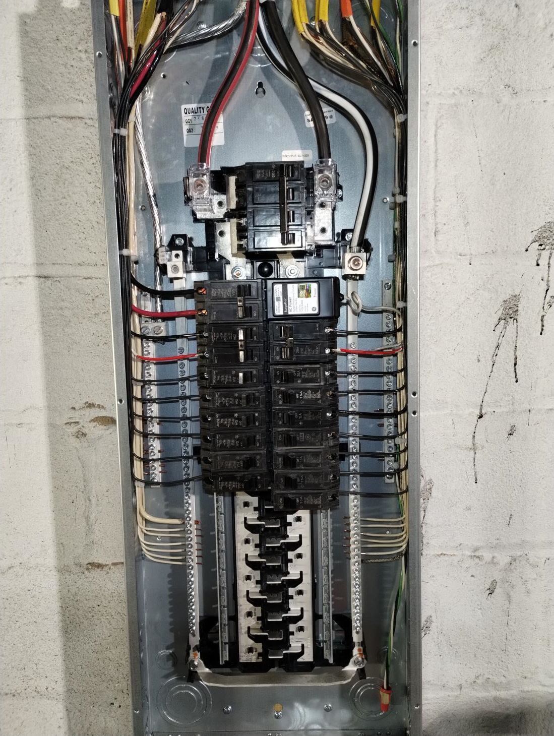 Electrical breaker panel with multiple circuit breakers and exposed colored wires in a gray metal box