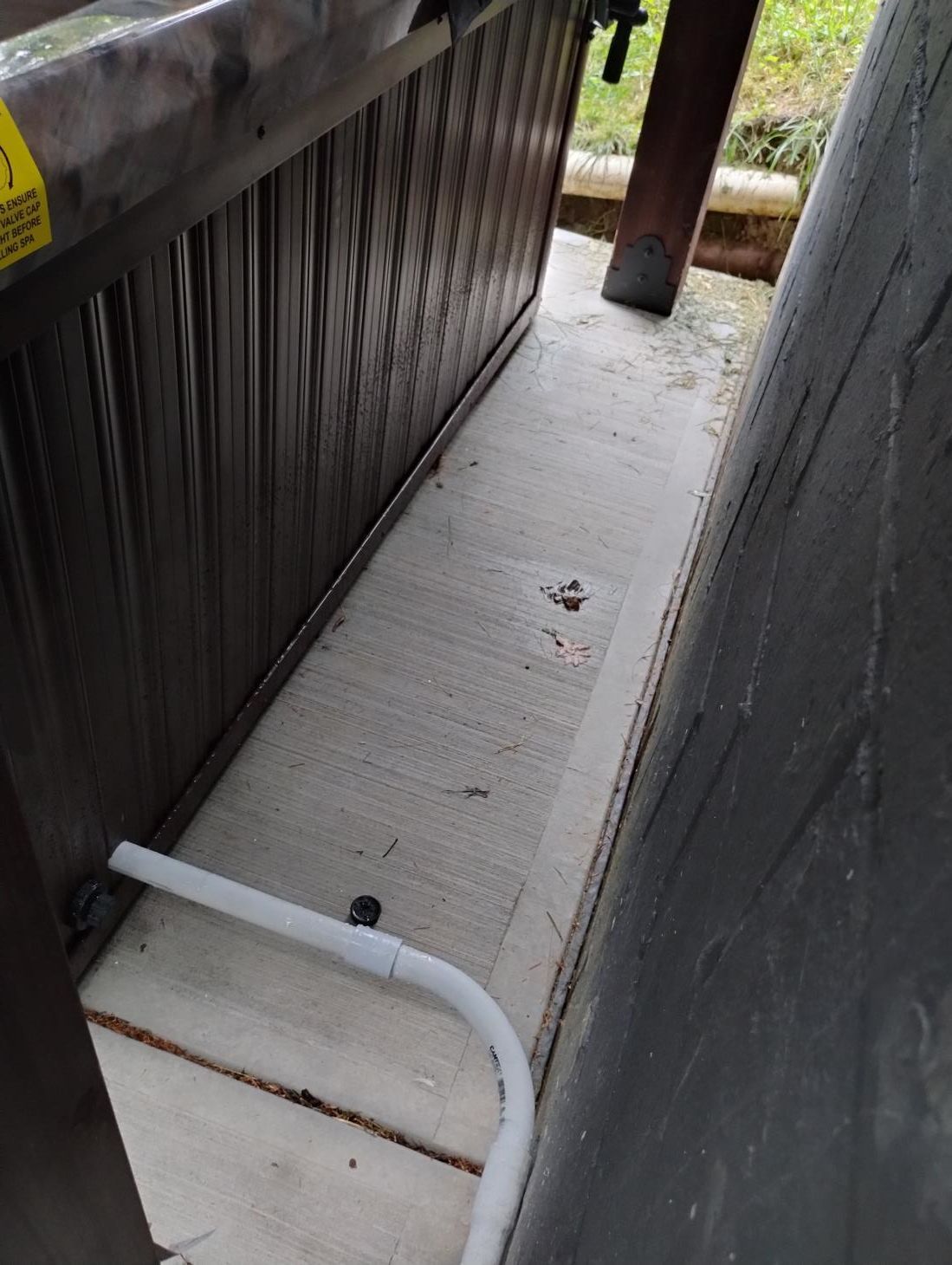 Narrow concrete walkway beside dark railing, with a white pipe on the floor and a wooden post ahead.