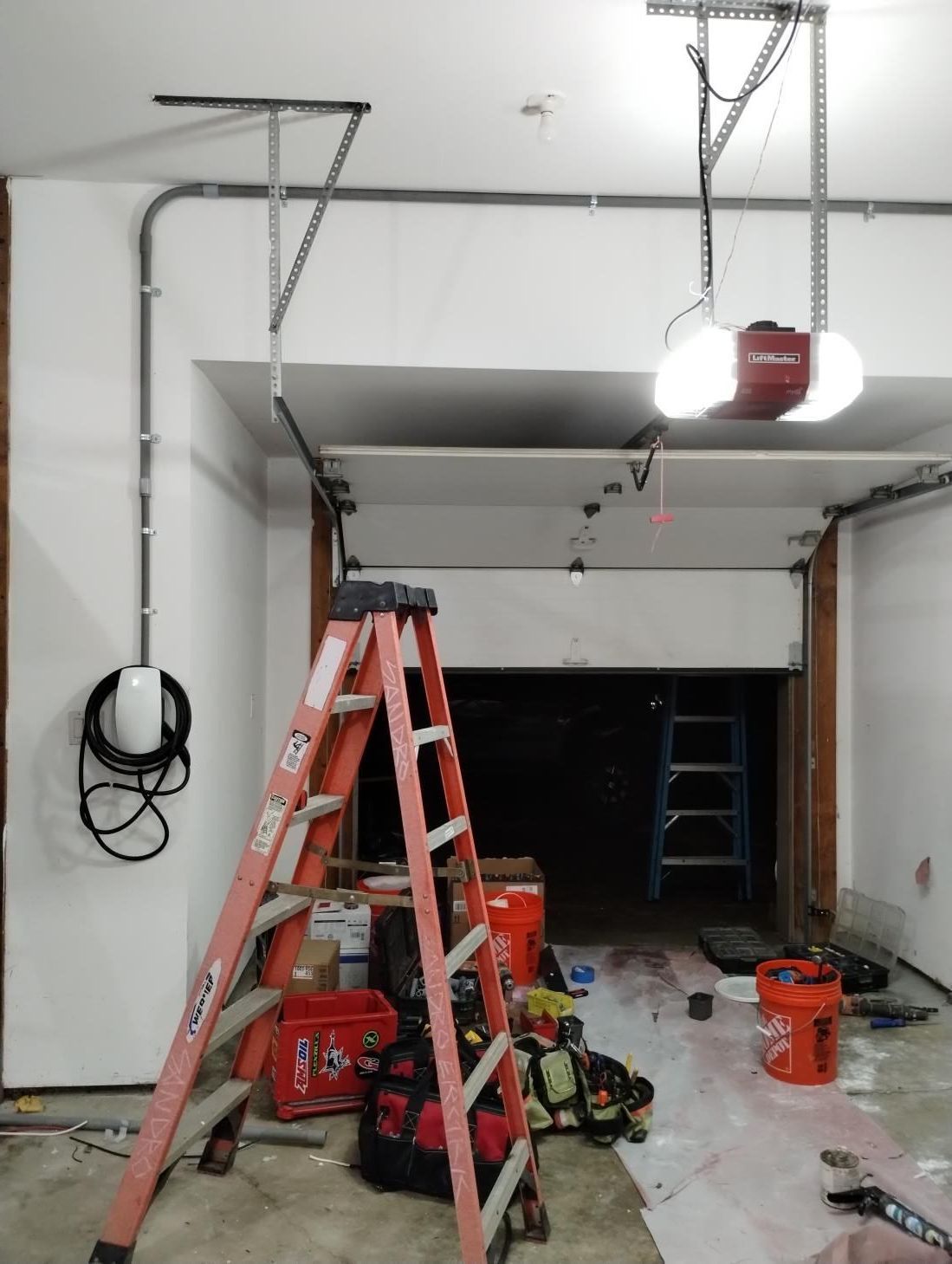 Garage under repair with ladders, tools, and a garage door opener installed on the ceiling