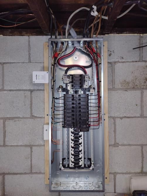 Open electrical breaker panel in unfinished basement wall with exposed wiring.