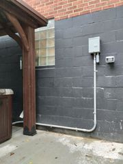 Gray exterior wall with electrical box and conduit beside a wooden post and patio area