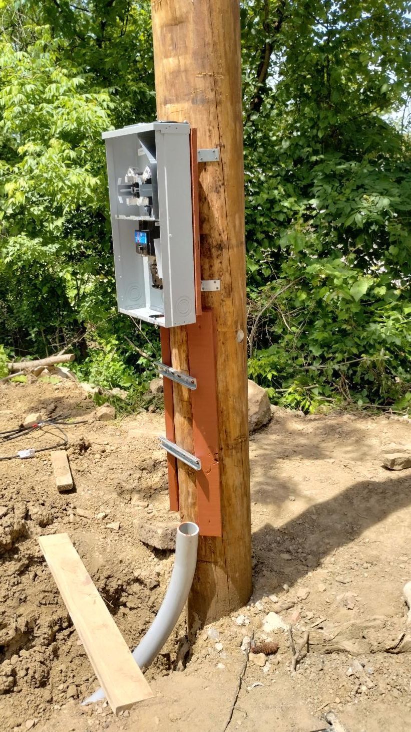 Electrical meter and conduit mounted on a wooden utility pole at a dirt construction site.