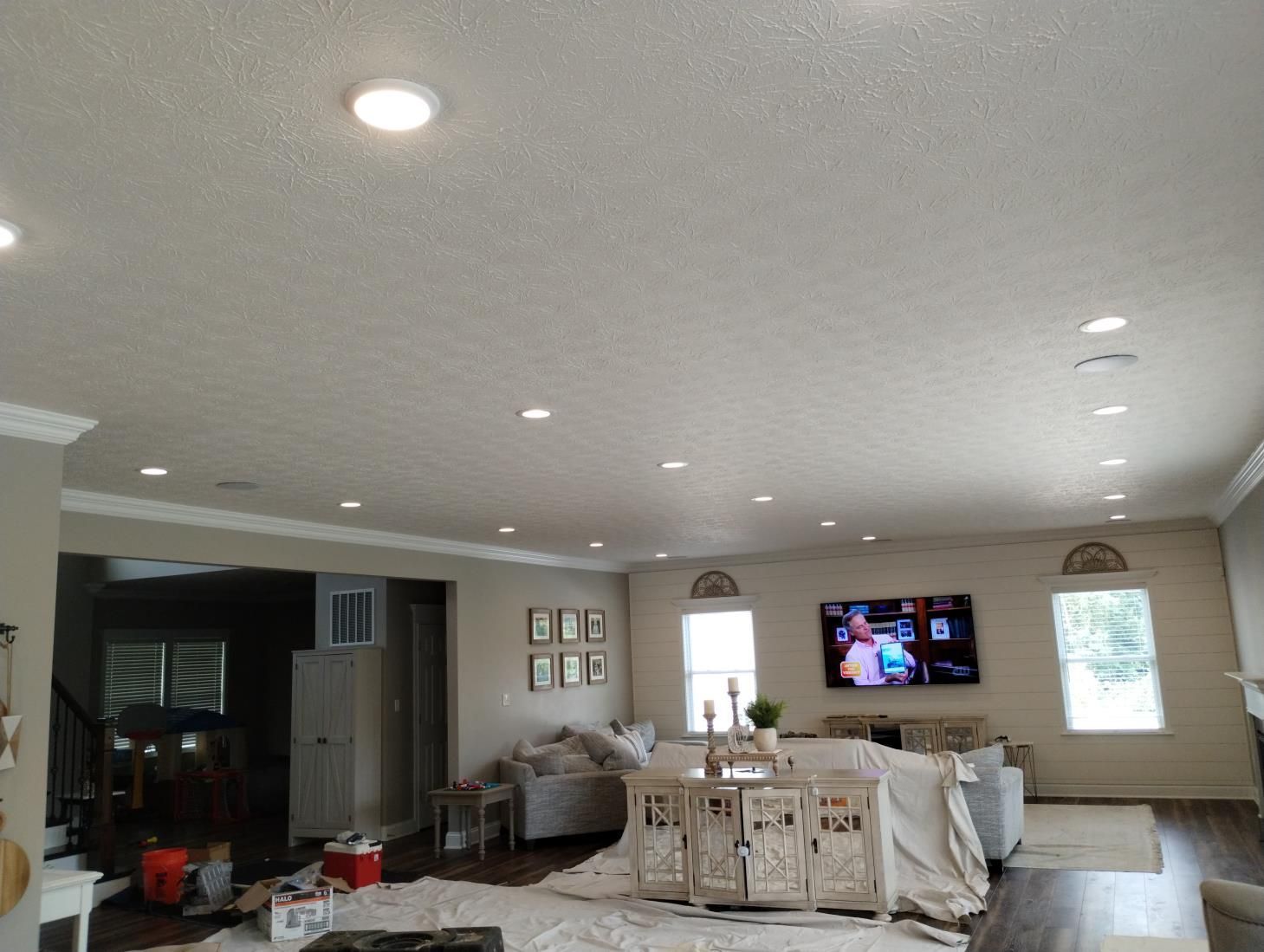 Spacious living room with white furniture, wall-mounted TV, recessed lights, and bright windows