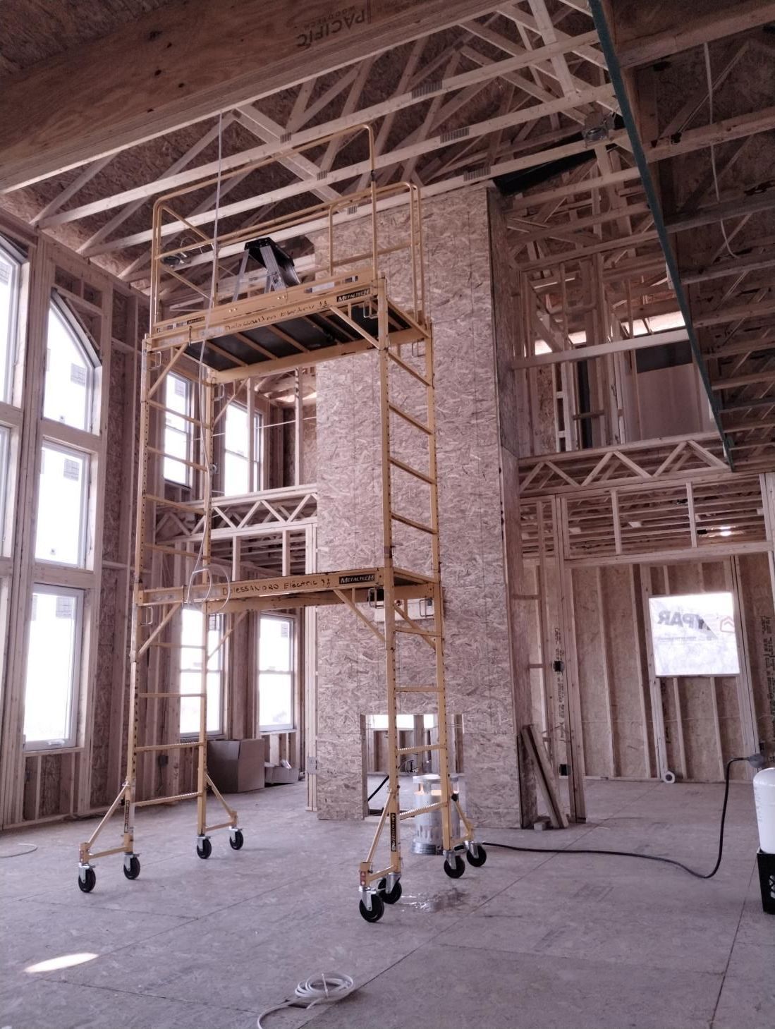 Scaffolding inside an unfinished wood-framed building with exposed beams and tall windows