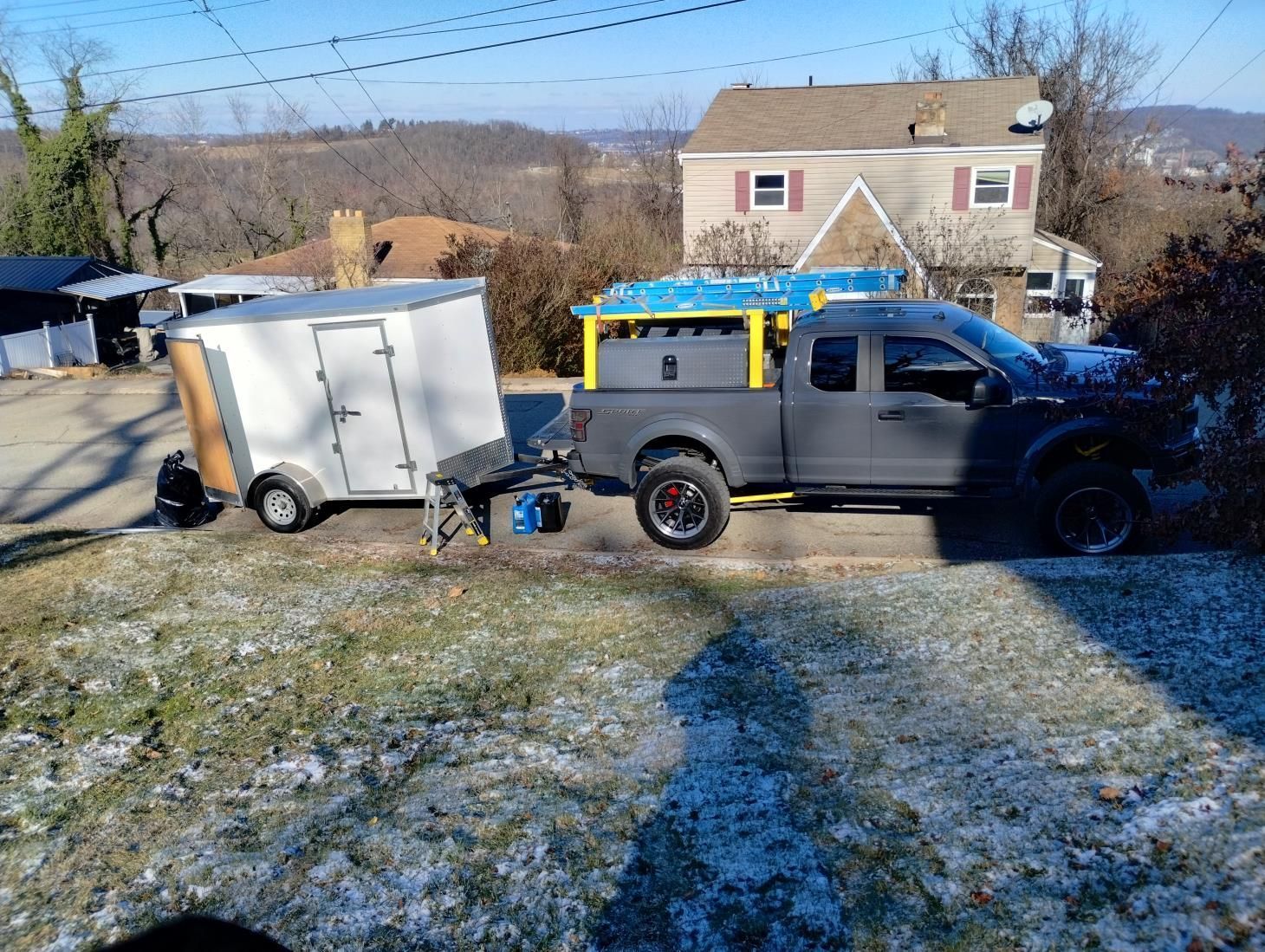 Pickup truck towing a white trailer on a snowy driveway in front of a house