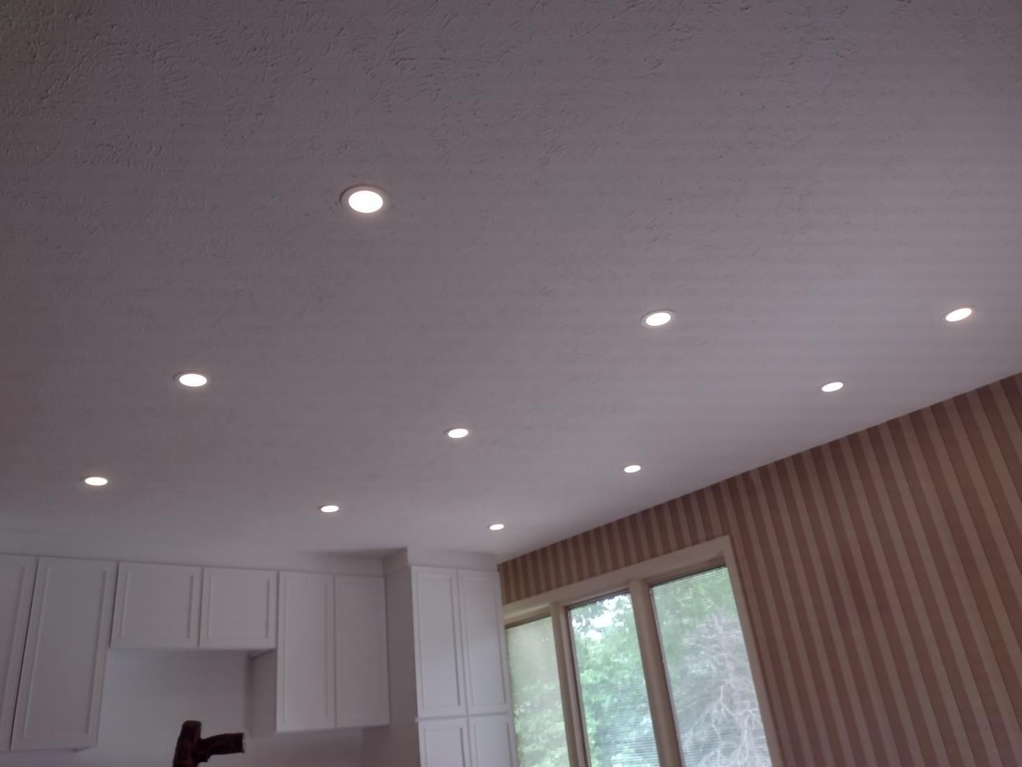 White ceiling with recessed lights above a room and large windows.