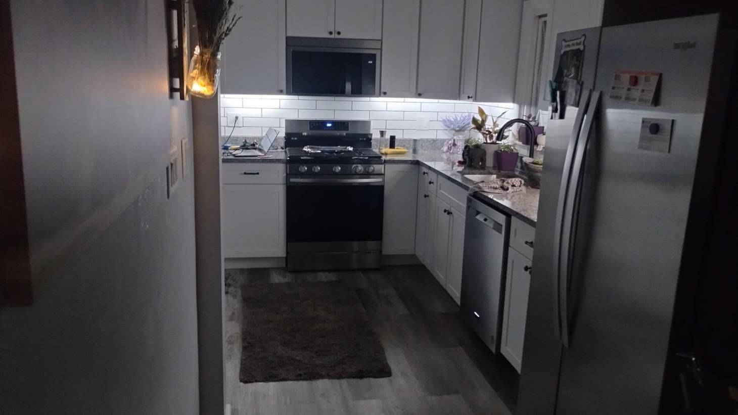 Modern kitchen with stainless steel appliances, white cabinets, and a dark rug on wood flooring.