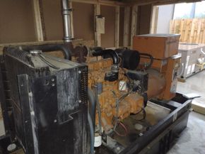 Industrial generator set with black radiator and orange engine inside a utility room