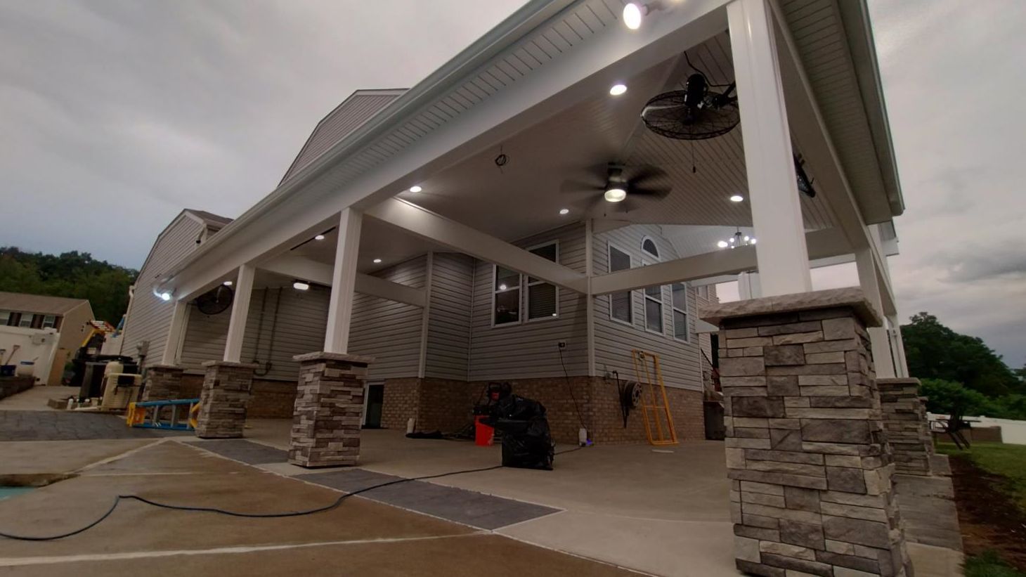 Covered patio with stone columns, ceiling fans, and concrete flooring in a modern outdoor living area
