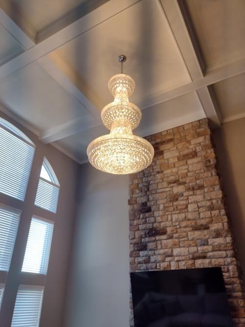 Crystal chandelier hanging from a vaulted ceiling above a stone fireplace in a bright living room
