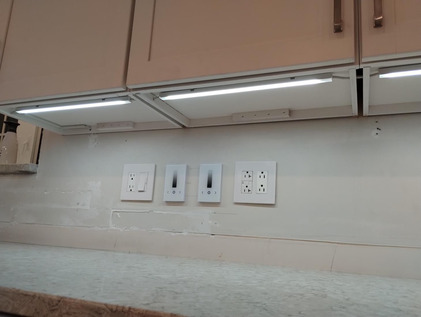Kitchen backsplash with electrical outlets and under-cabinet lights above a light countertop