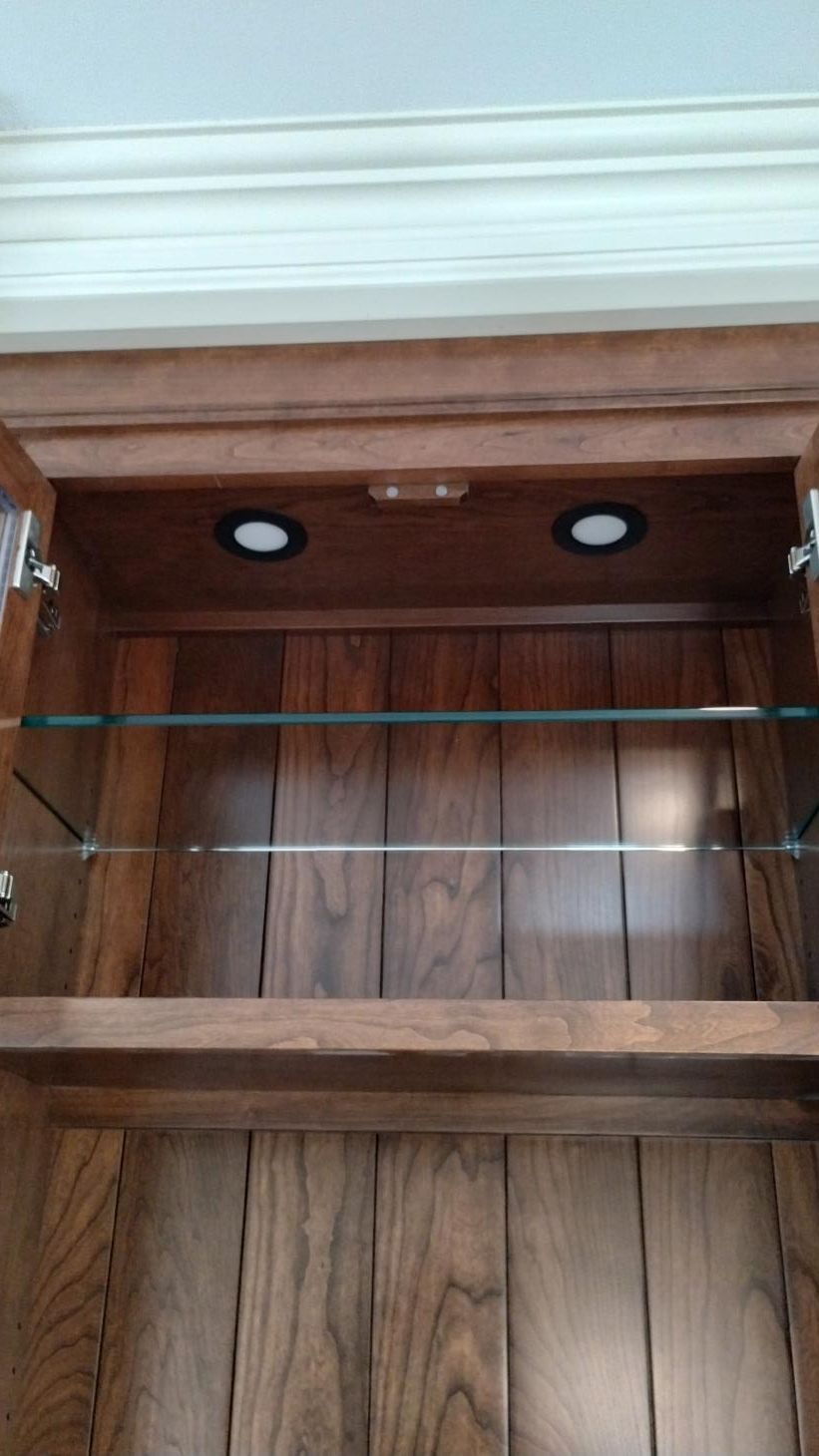 Open wooden cabinet with two shelves and built-in lights under a white crown molding.