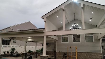House exterior with covered porch, lit ceiling, and stone columns under an overcast sky
