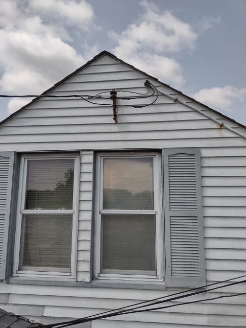 House gable with white siding, two windows, and overhead power lines against a cloudy sky