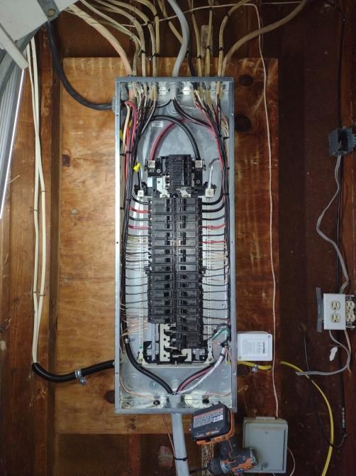 Open electrical breaker panel with exposed wiring on a wooden wall.