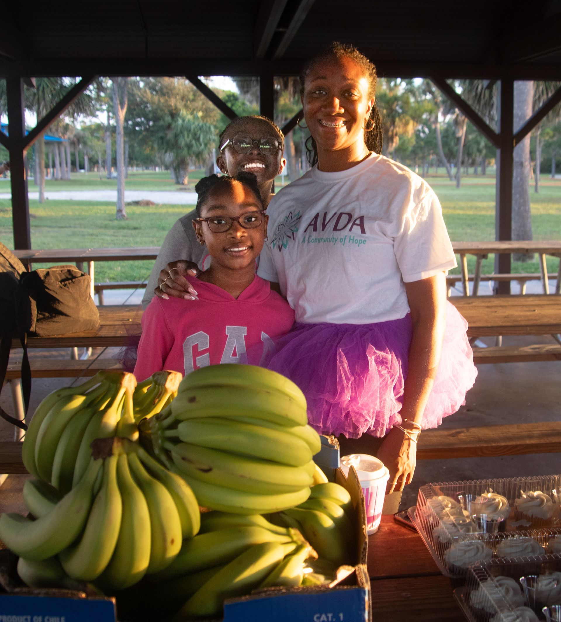 A woman wearing an avda shirt stands next to a girl
