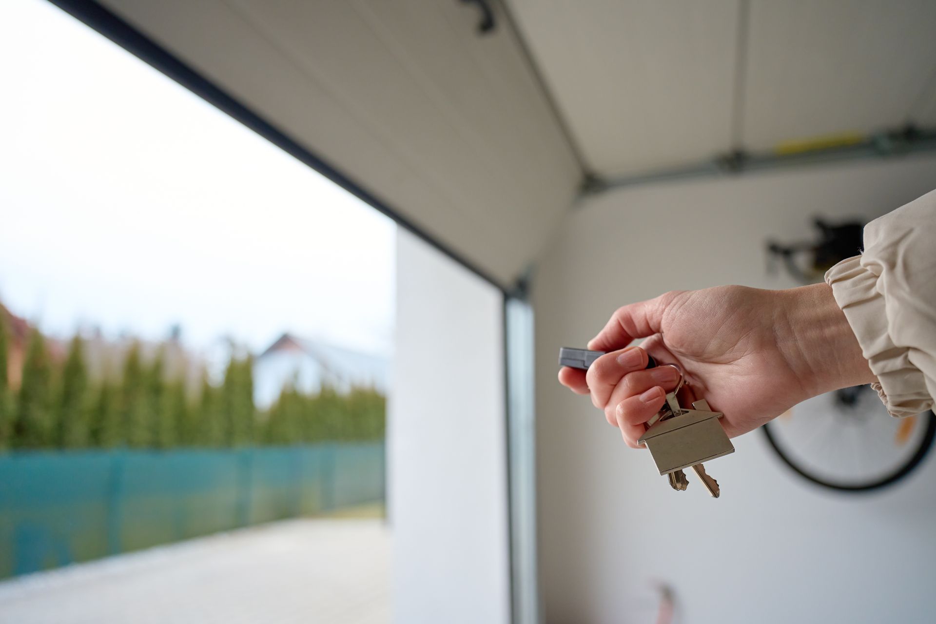 Close-up of hand holding garage remote and keys inside garage with open door.