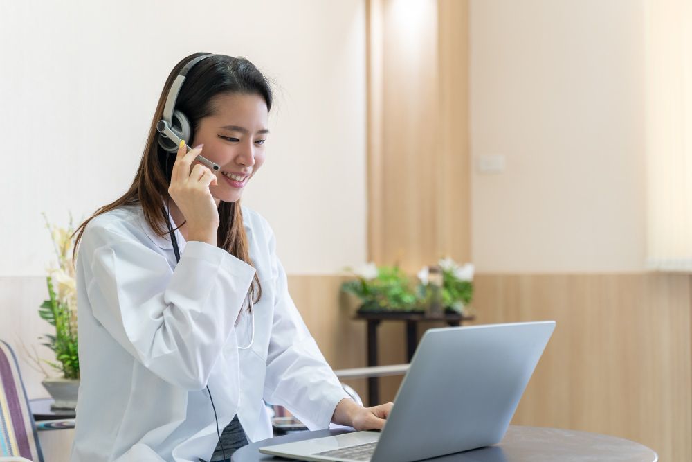 A woman is sitting at a table with a laptop and talking on a cell phone.