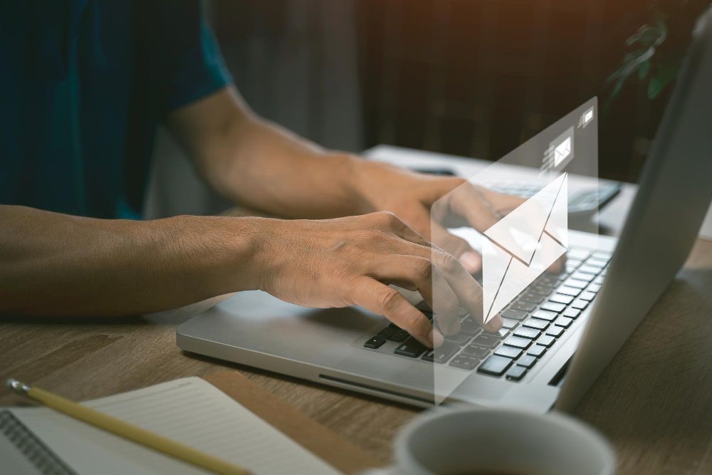 A man is typing on a laptop computer with an envelope coming out of the screen.