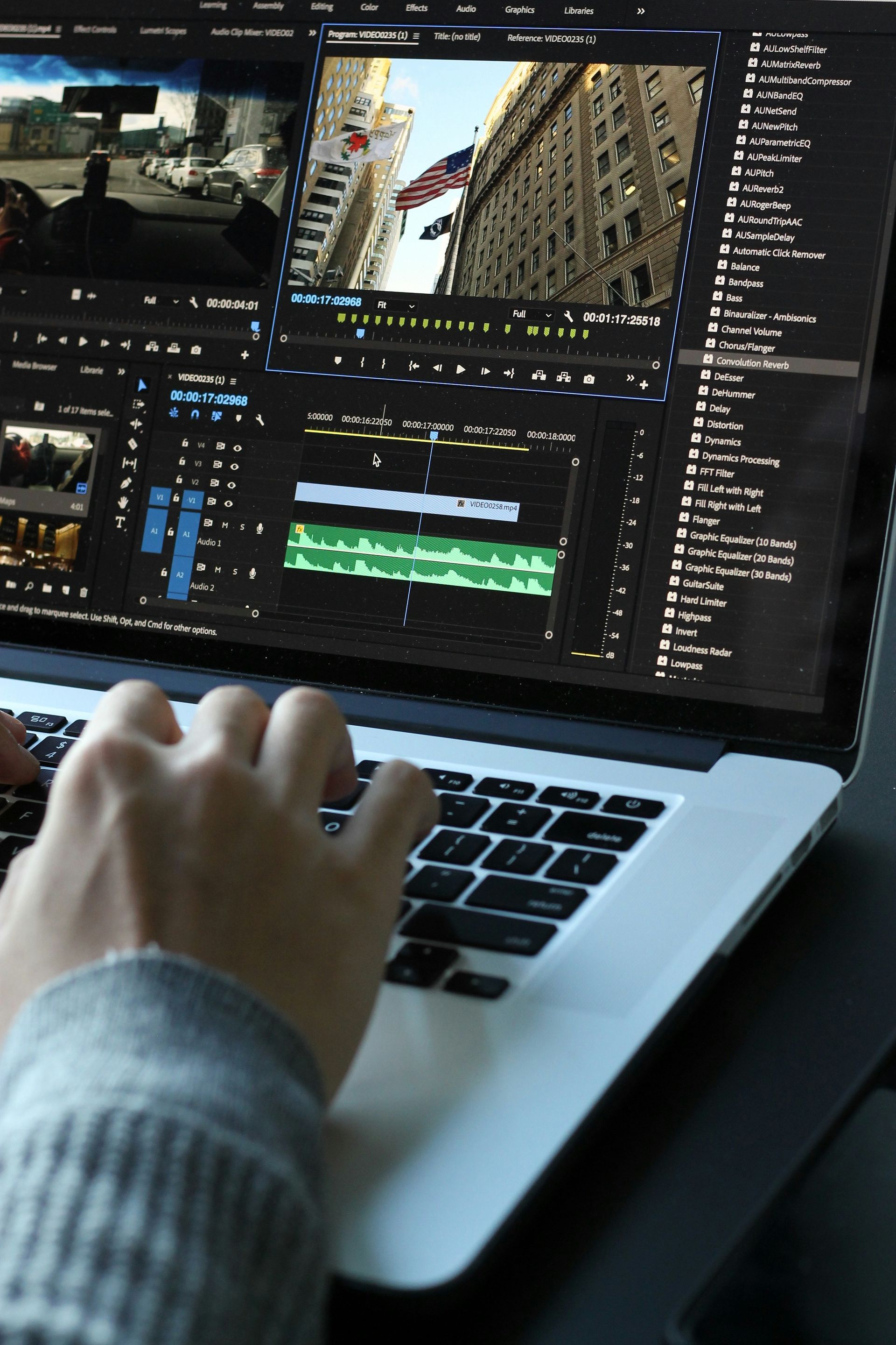 Hands typing on a laptop, editing a video with a city scene on screen.