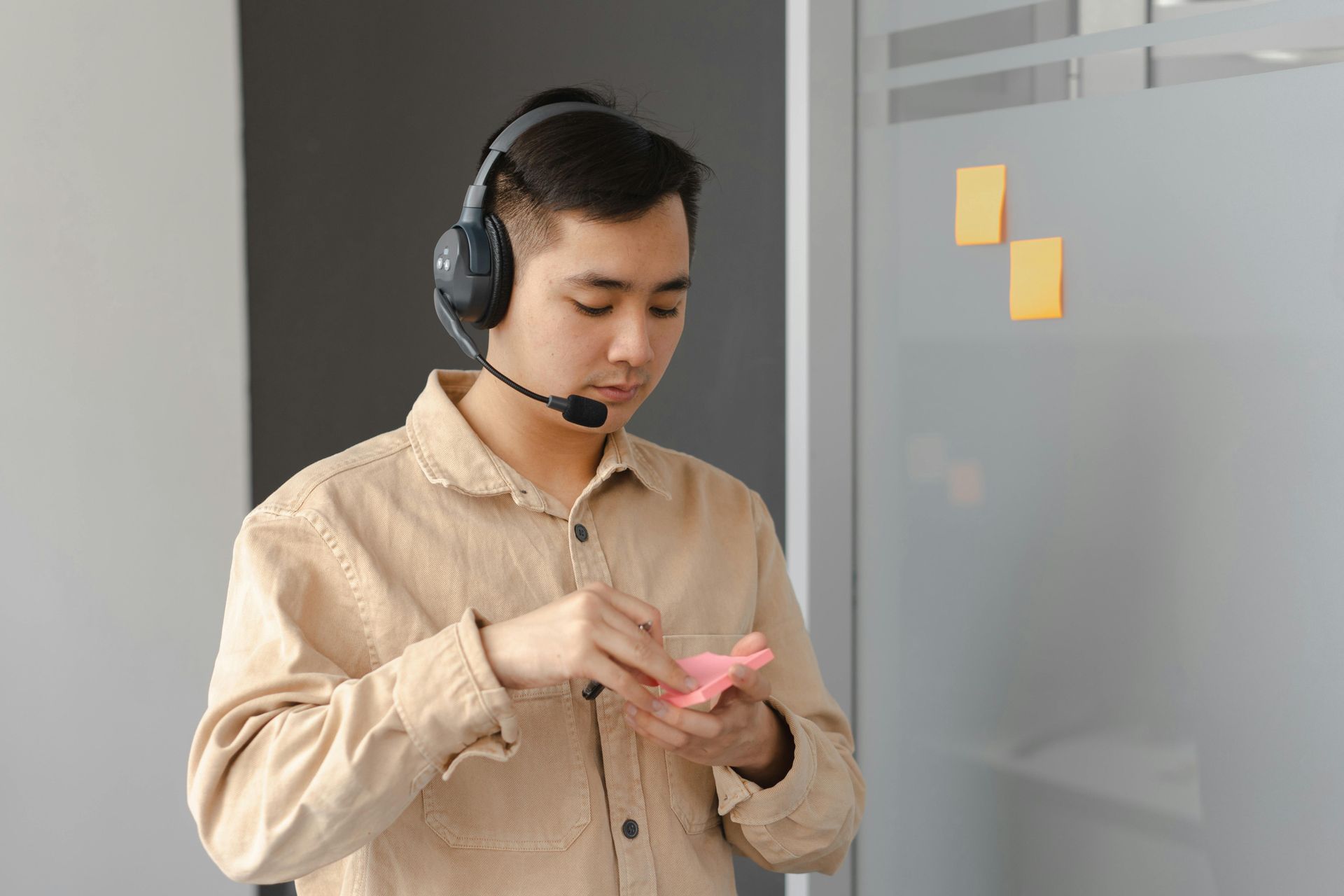 A man wearing headphones and a microphone is looking at a cell phone.